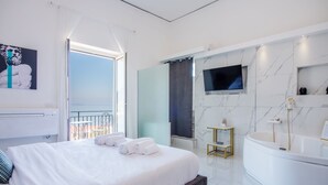 A modern hotel room with a large bed, a bathtub, a TV, and a balcony with a view. - Naro Suites and Rooms (Bacoli)