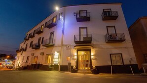 A multi-story hotel with balconies, a well-lit entrance, and a visible sign indicating a restaurant. - Naro Suites and Rooms (Bacoli)