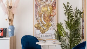 A room with a white desk, two blue velvet chairs, a large poster, a vase with dried plants, and a tall green plant. - Naro Suites and Rooms (Bacoli)