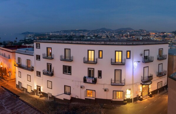 Ein mehrstöckiges Hotel mit Balkonen, einer Straße davor und einer Aussicht auf Stadt und Berge im Hintergrund.