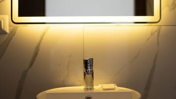 Um banheiro moderno com uma pia redonda, um espelho iluminado e parede de mármore.