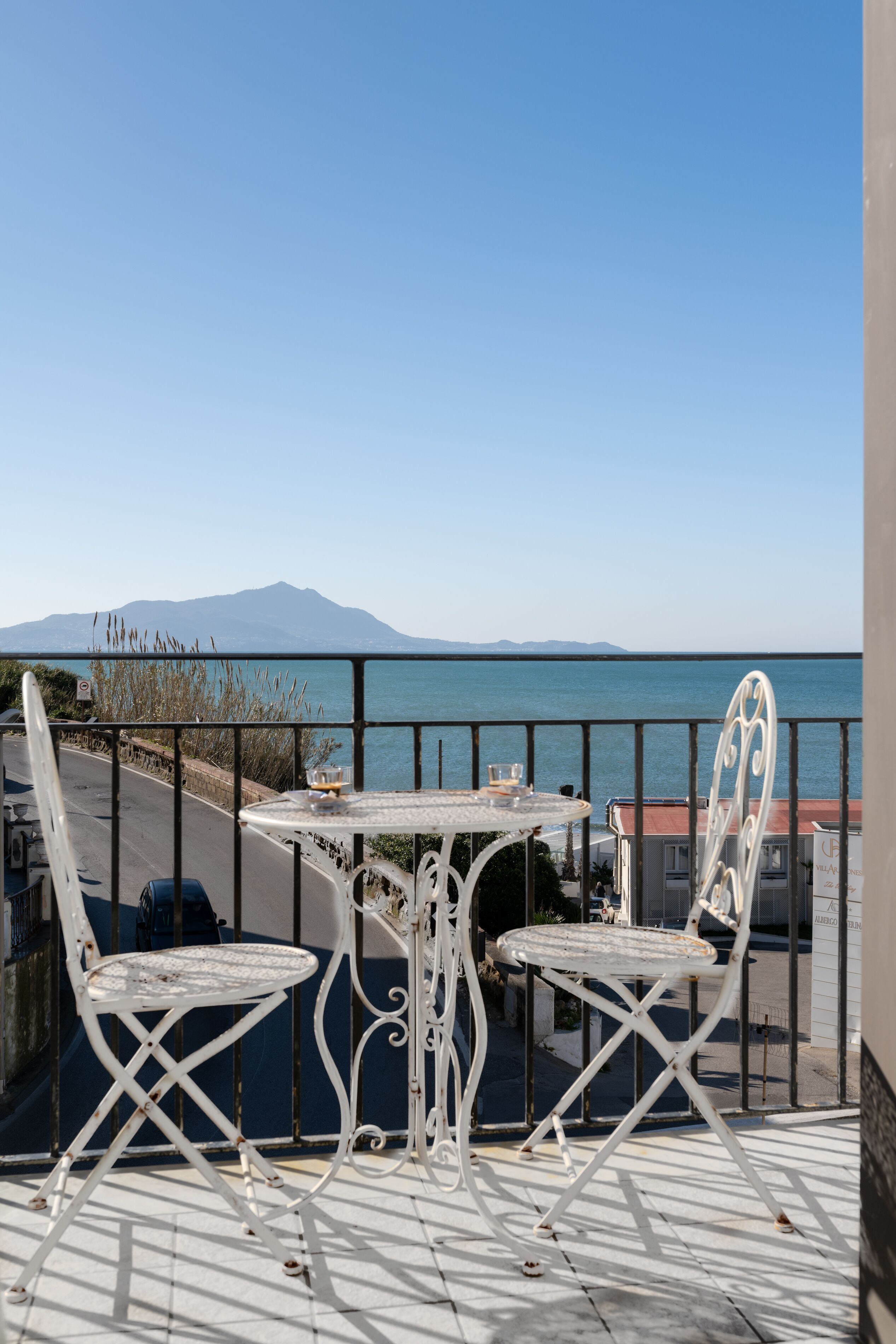 Un balcon avec deux chaises en métal blanc et une petite table, d’où l’on peut admirer un plan d’eau et des montagnes lointaines.
