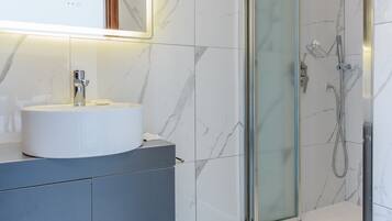 Un bagno moderno con pavimento in marmo, un lavabo bianco con uno specchio sopra e una cabina doccia in vetro.