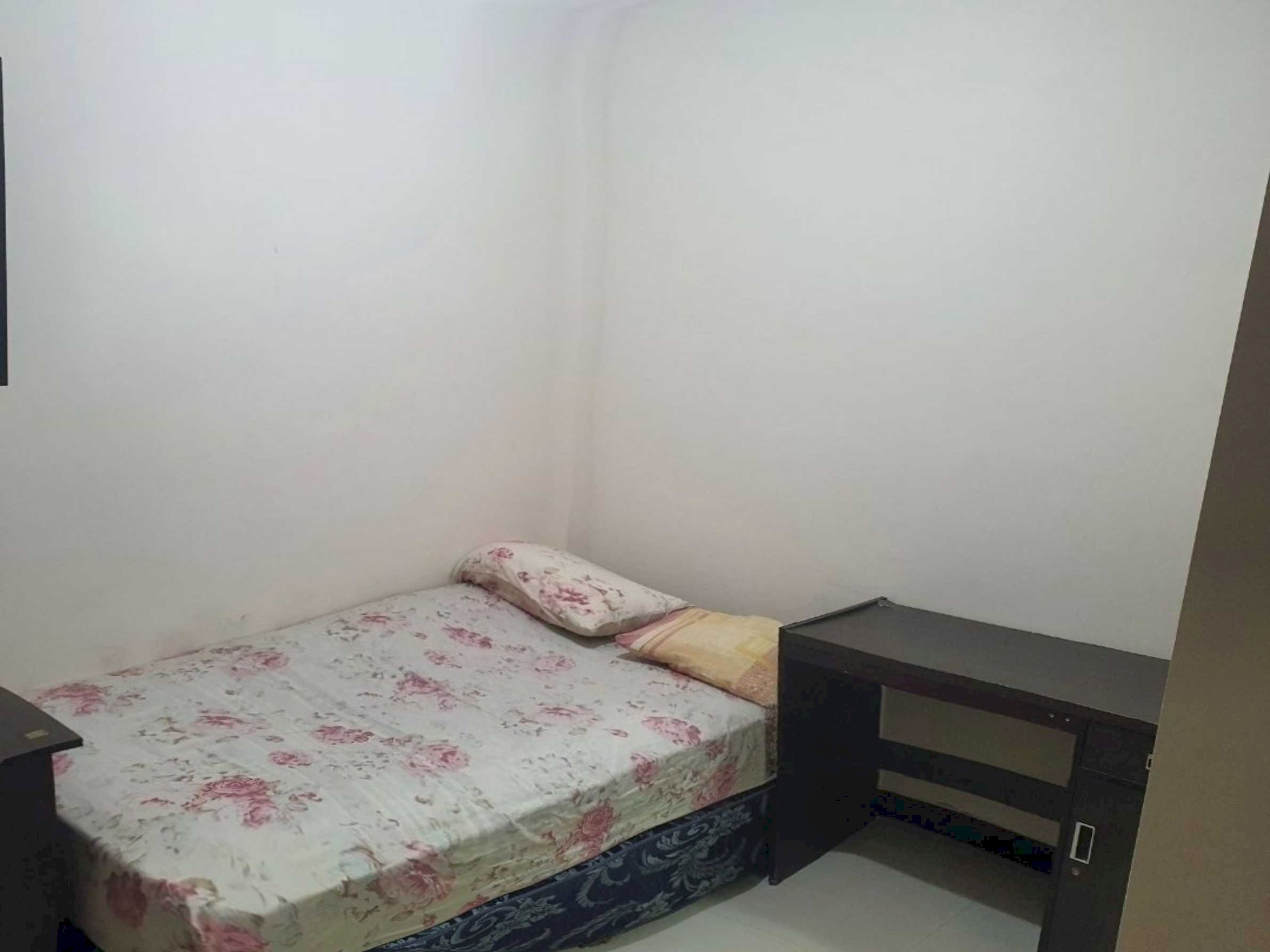 A small, single-bed room with a floral bedspread, a bedside table, and a wardrobe.