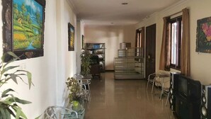 A hotel lobby with a long reception desk, a glass partition, a TV, and a seating area with chairs and a table. - OYO Life 93202 Pentagon Homestay Syariah (Surabaya)