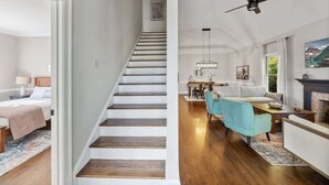 A staircase leading to a bedroom with a bed and nightstand, a dining area with a table and chairs, and a living room with a sofa and fireplace.