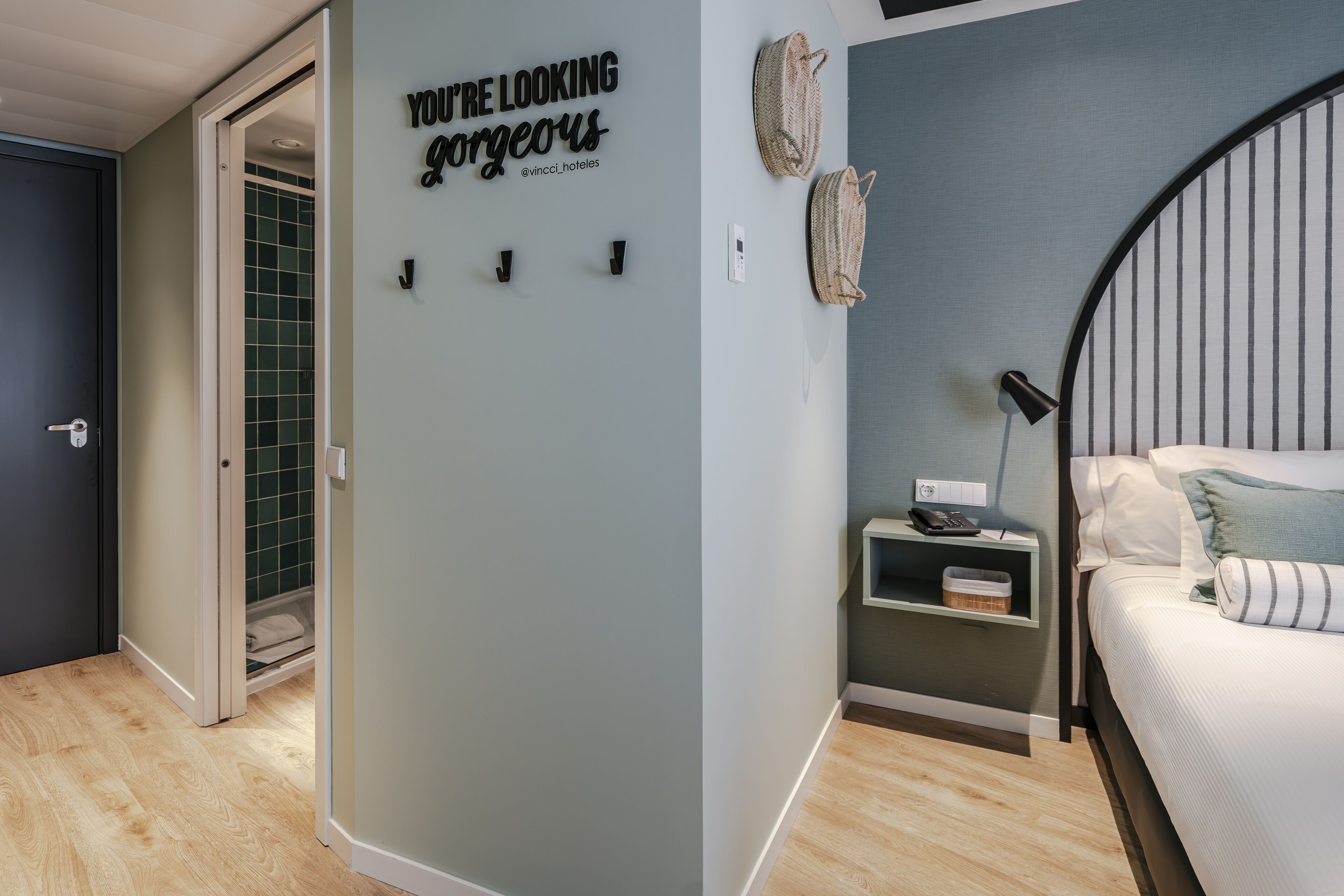 A bedroom with a bed, a nightstand, a wall-mounted lamp, and a decorative sign.