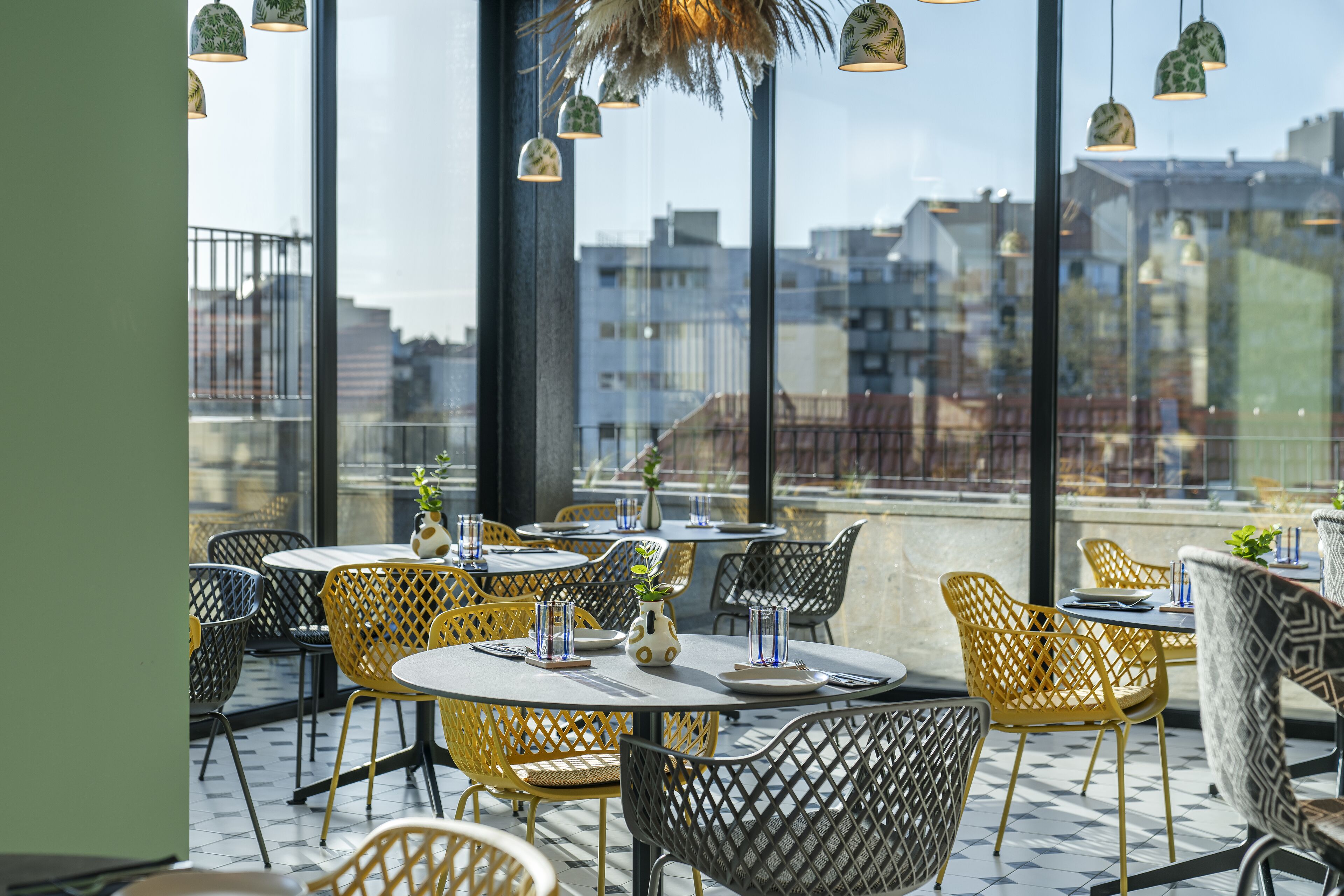 A rooftop restaurant with outdoor seating, large windows, and hanging pendant lights.