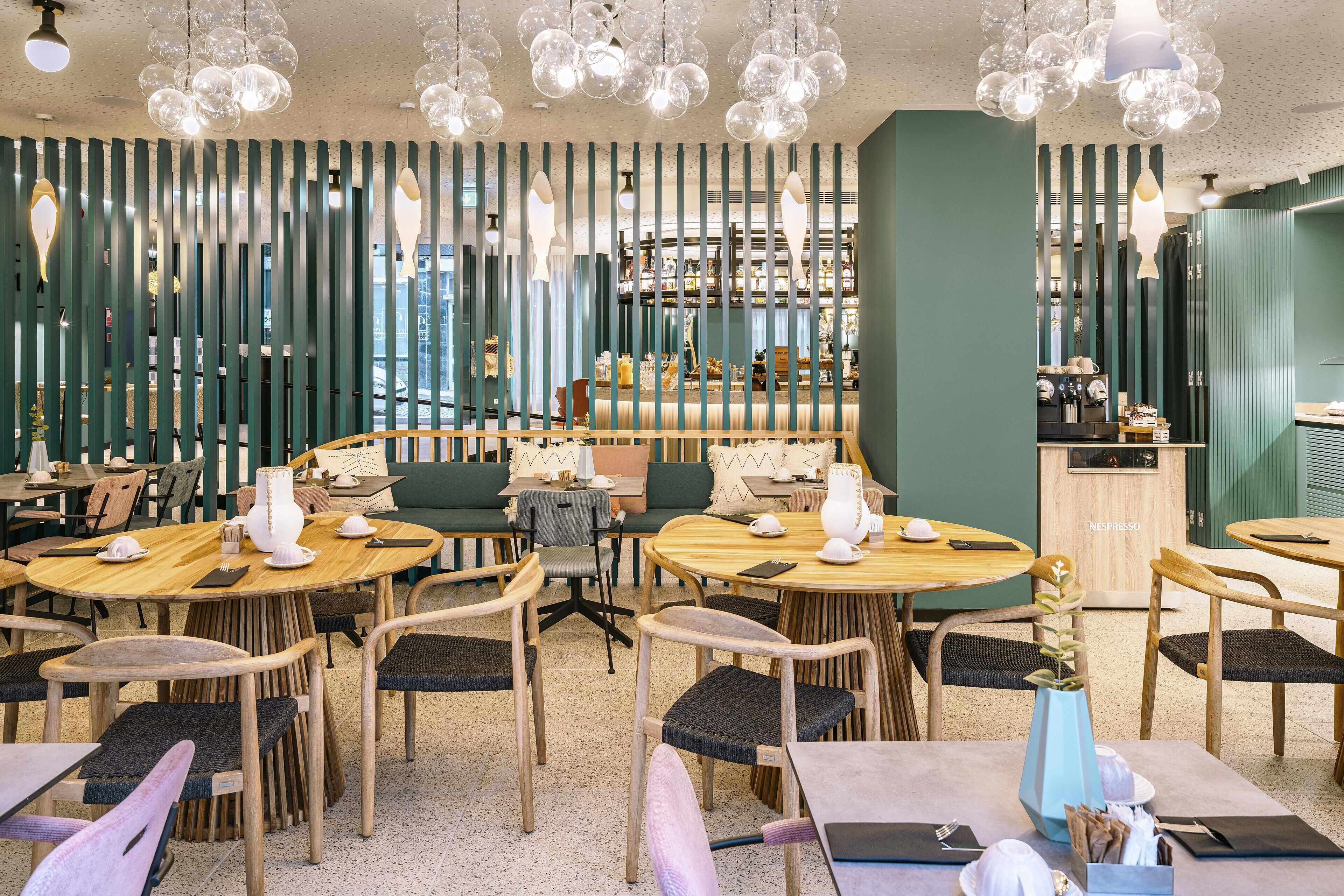 Un interior de restaurante moderno con mesas redondas, sillas de madera y lámparas colgantes esféricas.