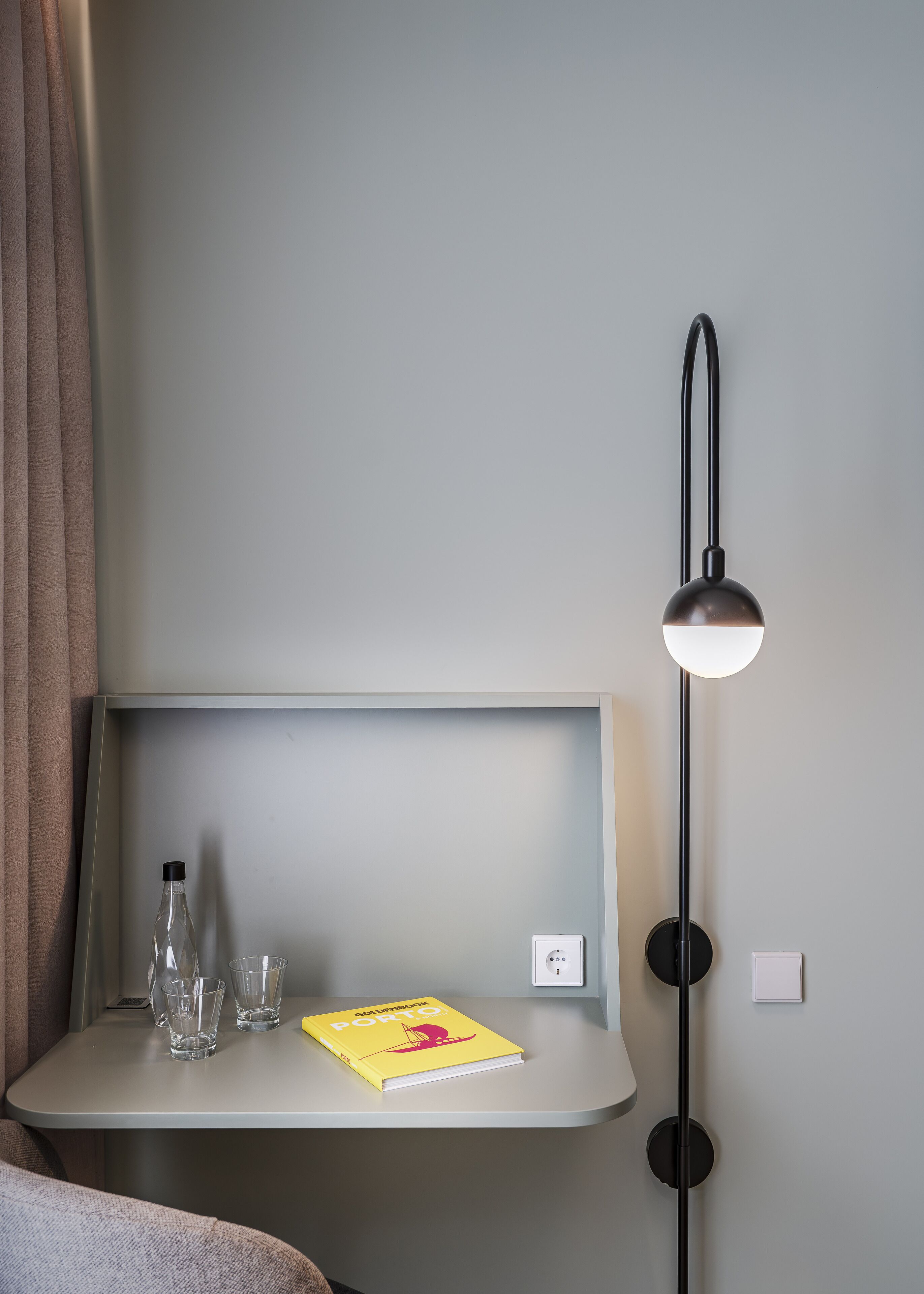Ein Hotelzimmer mit Nachttisch, einem Buch mit dem Titel 'Goldenbloom Porto', zwei Gläsern und einer Flasche.