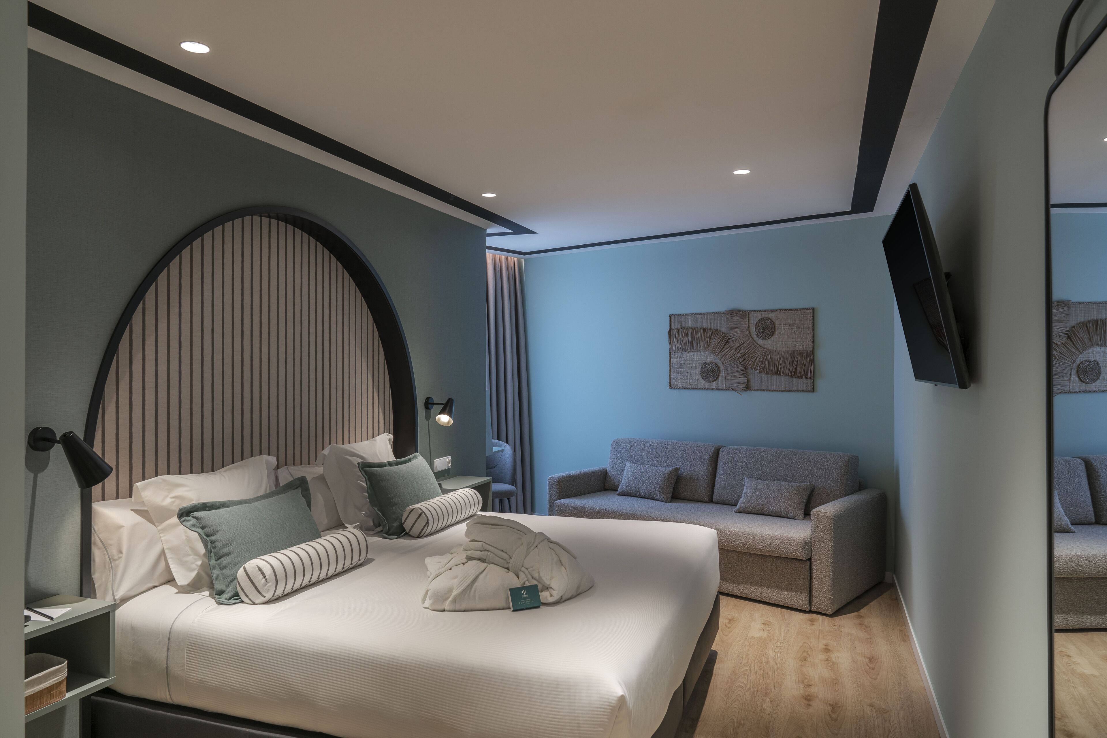 Une chambre d’hôtel moderne avec un grand lit, un canapé, un téléviseur fixé au mur et un élément décoratif mural.