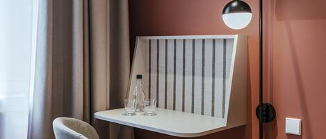 Een hotelkamer met een bed, een bureau met lamp, een aan de muur bevestigde televisie en een raam met gordijnen.