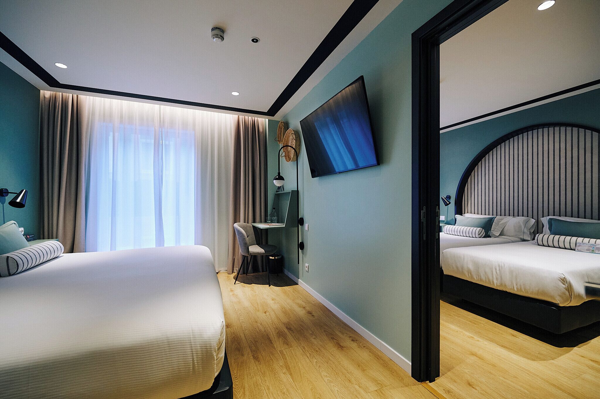 A modern hotel room with two beds, a desk, and a large TV.