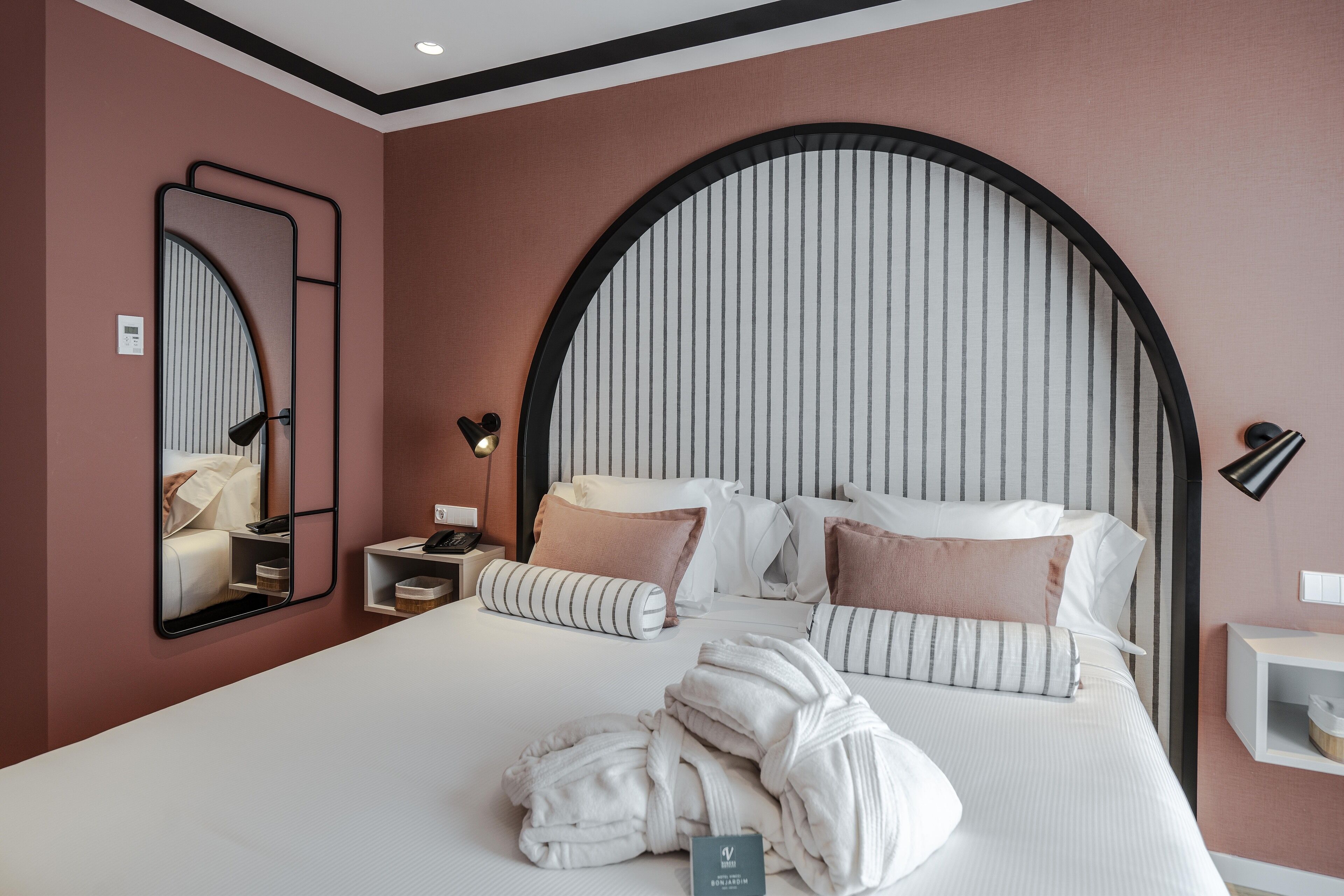 Quarto de hotel moderno com uma cama grande, um espelho, mesa de cabeceira e criado-mudo.