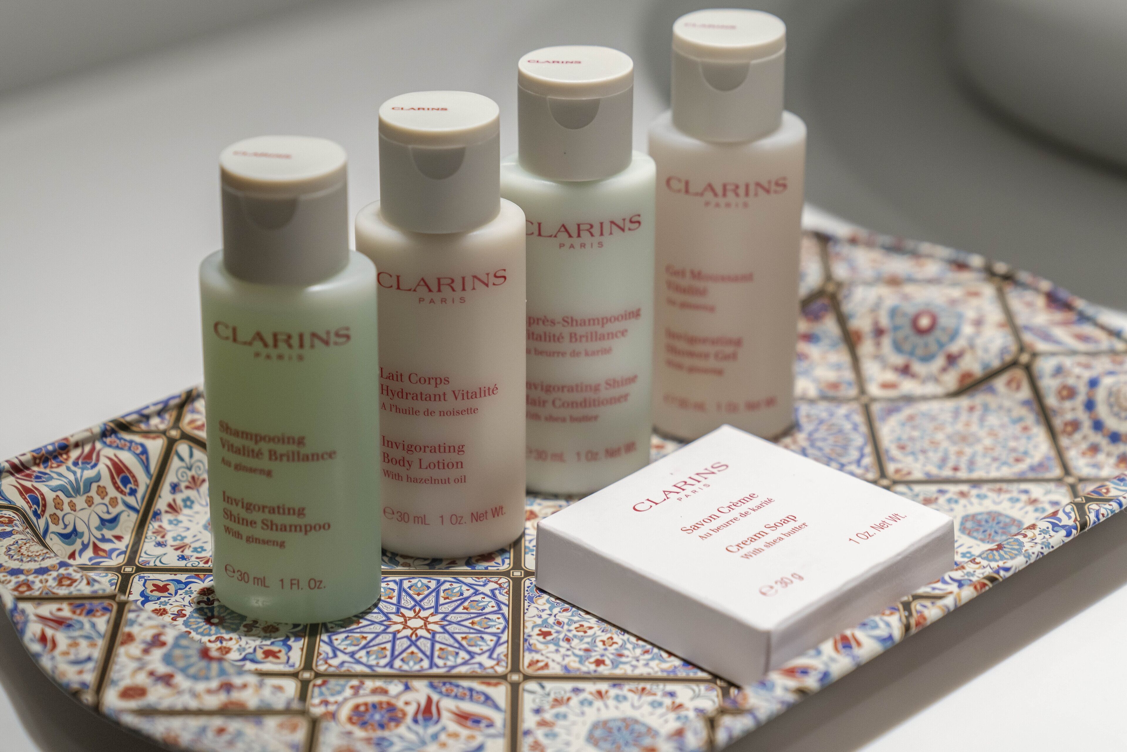 Four Clarins Paris skincare bottles and a box of Clarins body lotion on a patterned tile surface.