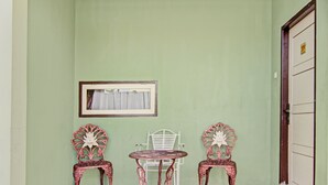 A room with a green wall, a white chair, a wooden table, and two ornate chairs.