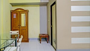 A room with a glass table, white chairs, a wooden wardrobe, and a small wooden stool.