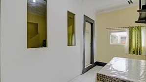 A room with a bed, a window with curtains, a door, and a small window with a view of the outside.