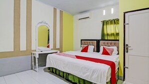 A hotel room with a bed, a bedside table, a mirror, and an air conditioning unit.