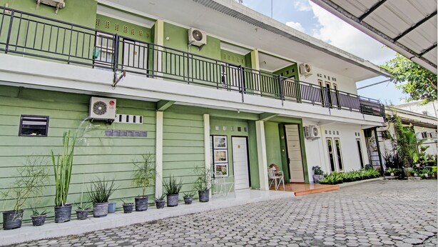 A green building with multiple balconies, potted plants, and a tiled entrance.