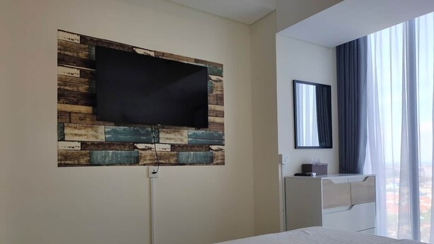 Ein Hotelzimmer mit Bett, einem Wand-Fernseher, einem Nachttisch und einem Fenster mit Vorhängen.