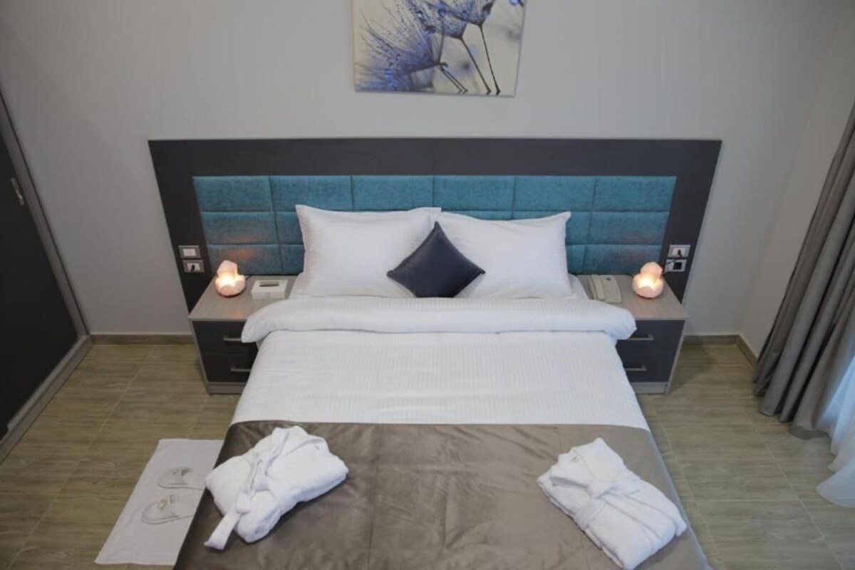 A hotel room with a bed, bedside tables, and a nightstand with a lamp.