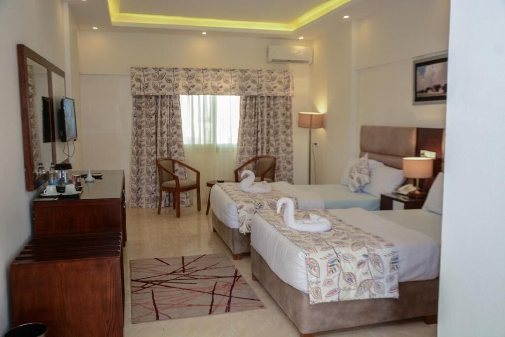 A hotel room with two beds, a desk, a chair, a TV, and a window with curtains.