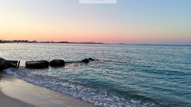 Une scène de plage avec une eau calme et un coucher de soleil.