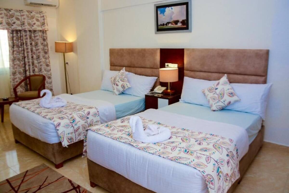 Two twin beds with matching headboards, a bedside lamp, and a chair in a hotel room.