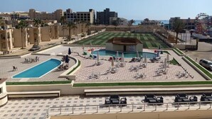 Un espace piscine doté de chaises longues et de parasols, entouré de bâtiments et surplombé par un ciel dégagé.