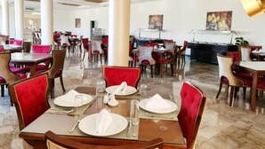 Un restaurant d’hôtel doté de nombreuses tables, de chaises à revêtement rouge et d’un sol en marbre poli.