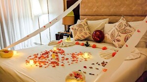 Un lit bien fait, décoré de pétales de rose et de bougies, une table de chevet avec une lampe et des coussins à motifs.