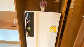 A white refrigerator with a digital display and a small flower on top, placed in a wooden cabinet. - Best Venue Hotel (Patong)