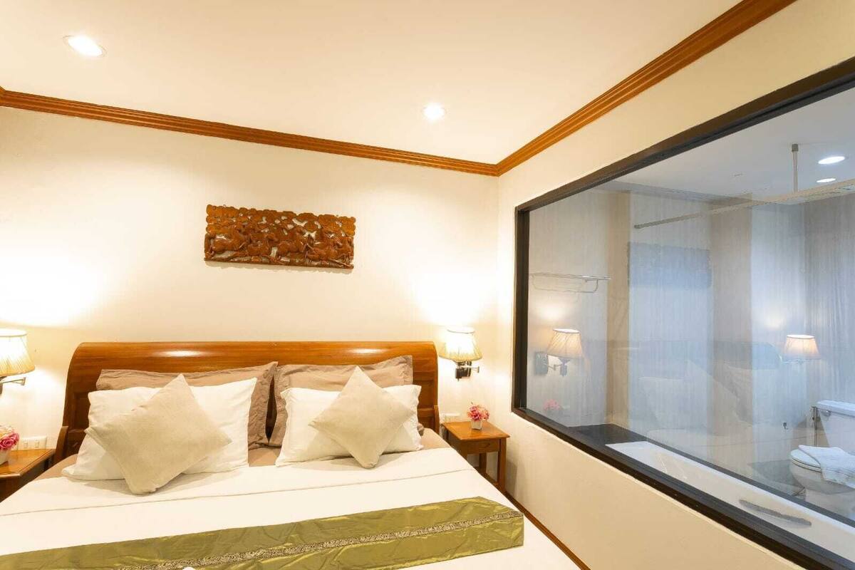 A hotel room with a large bed, two bedside lamps, a decorative wall piece, and a large window.