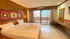 A hotel room with a large bed, a desk, and a view of buildings through the window. - Best Venue Hotel (Patong)