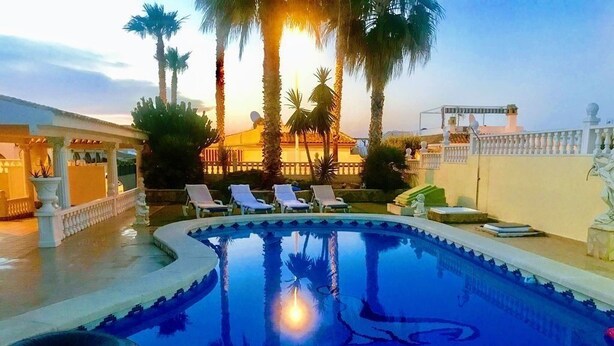Une piscine avec des chaises longues, des palmiers et un bâtiment en arrière-plan.