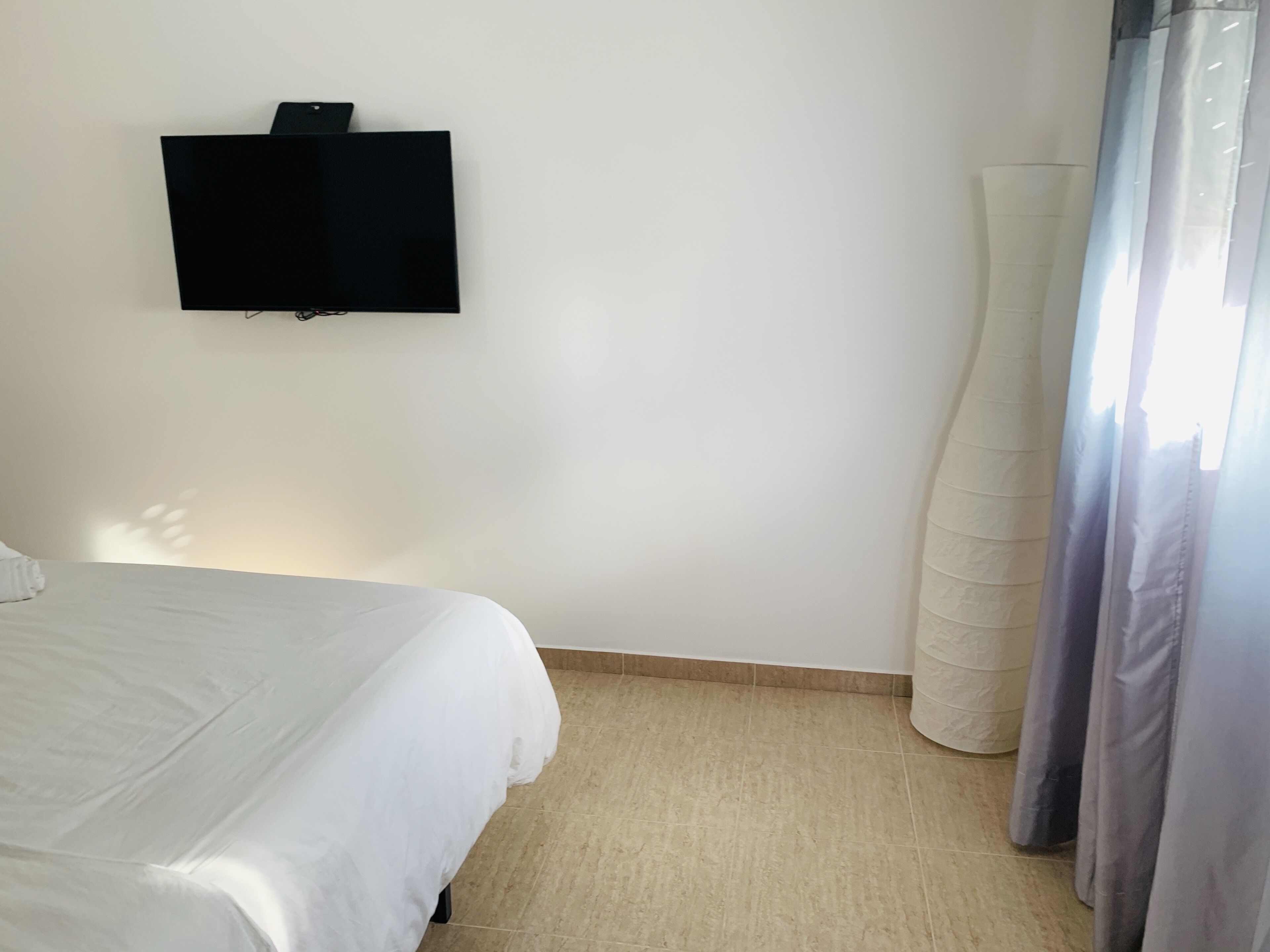 Ein Schlafzimmer mit einem Bett, einem an der Wand befestigten Flachbildfernseher und einem Fenster mit Vorhängen.