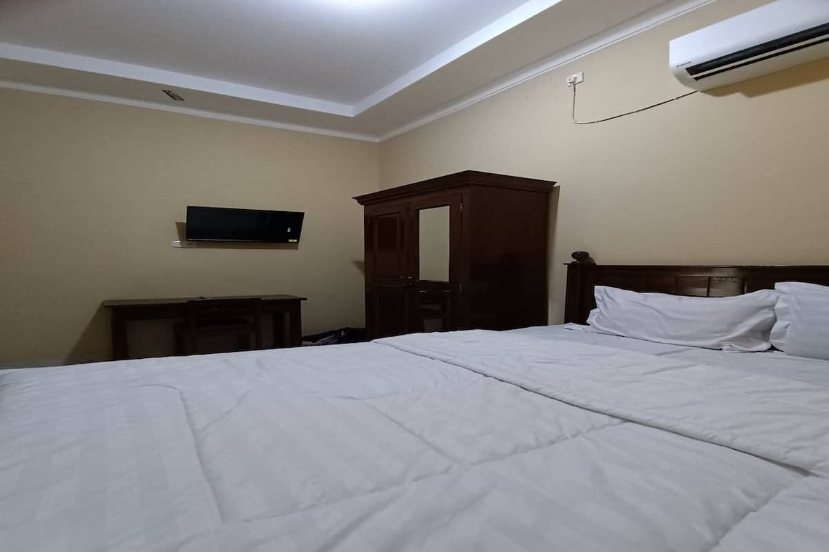 A hotel room with a bed, a wooden wardrobe, a television mounted on the wall, and an air conditioning unit.