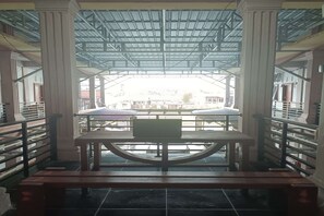 A covered outdoor seating area with a table and benches, surrounded by railings and columns. - Hotel O Merah House (Pekanbaru)
