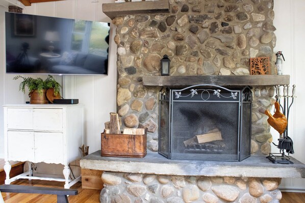 A stone fireplace with a metal screen, a mounted television, and a white cabinet with a plant. - 1000 FT to Assn Beach, Cute Cottage, Outdoor Dining (Lakeside)