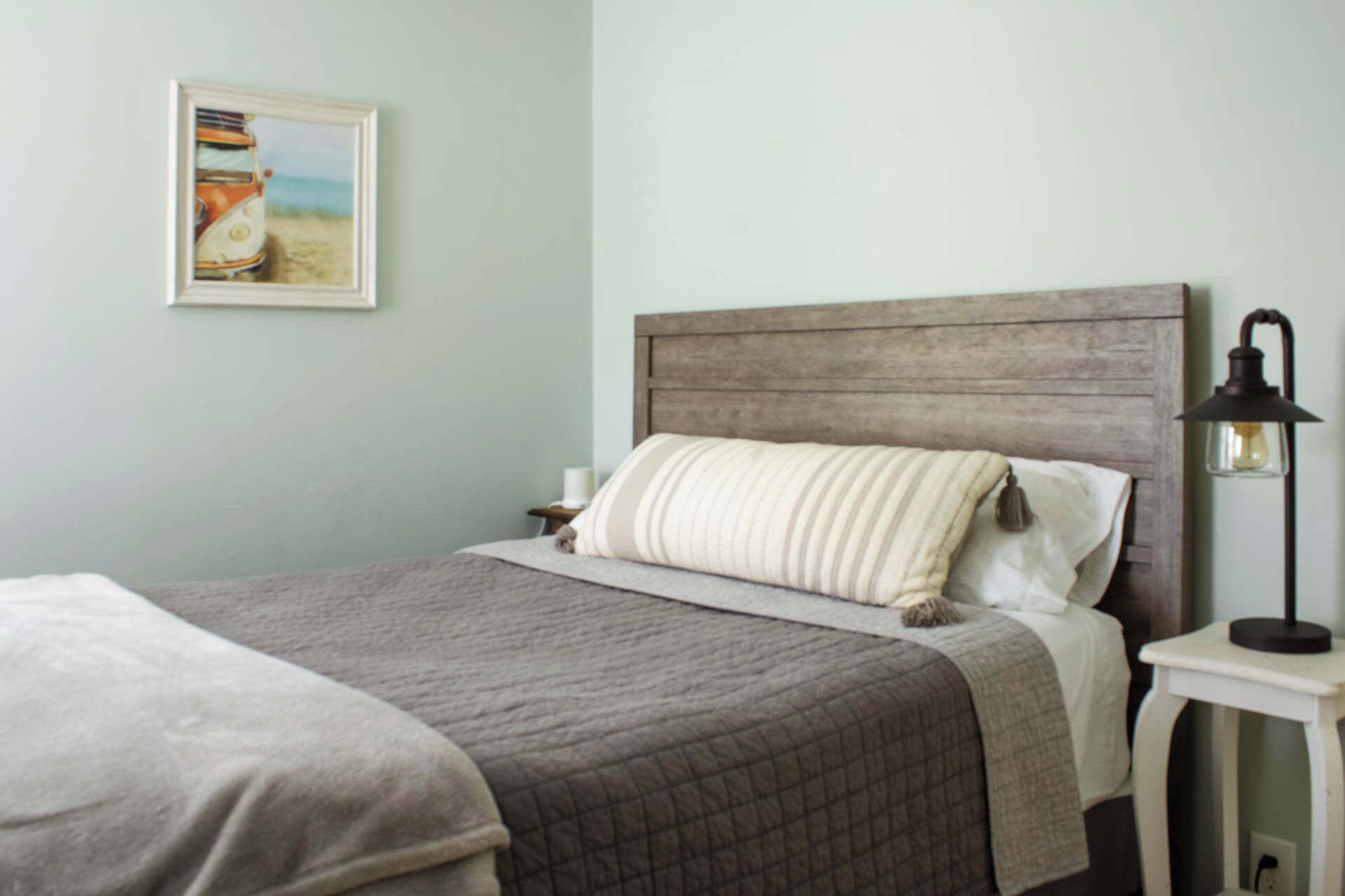 Una cama bien hecha con un edredón acolchado, un cabecero de madera y una lámpara de noche.