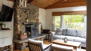 A cozy living room with a stone fireplace, wooden ceiling, and a comfortable sofa. - 1000 FT to Assn Beach, Cute Cottage, Outdoor Dining (Lakeside)