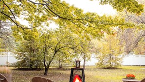 An outdoor seating area with a fire feature, surrounded by trees and a white fence. - 1000 FT to Assn Beach, Cute Cottage, Outdoor Dining (Lakeside)