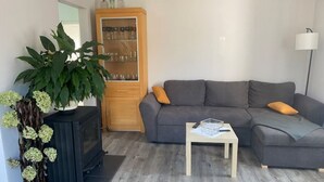 A living room with a grey sofa, a wooden cabinet with glassware, a black TV stand, and a potted plant. - Ferienhaus Albertus (Cottbus)
