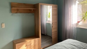 A bedroom with a wooden wardrobe, a bed, and a window with curtains. - Ferienhaus Albertus (Cottbus)