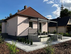A modern house with a sloped roof, a small porch, and a garden area with plants and a bench.