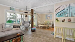 A living room with a sofa, a hanging chair, a dining table, and a kitchen area. - Three Bedroom Waterfront Home with a Rooftop Deck (Ocean City)