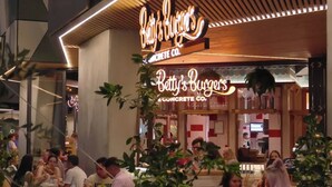 Un restaurante llamado 'Betty's Burgers' con un letrero de neón, mesas al aire libre y vistas al interior, incluyendo una barra y empleados.