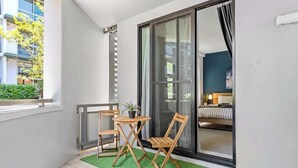 Un balcón con una pequeña mesa y dos sillas, una puerta corredera de vidrio y vista a un edificio.