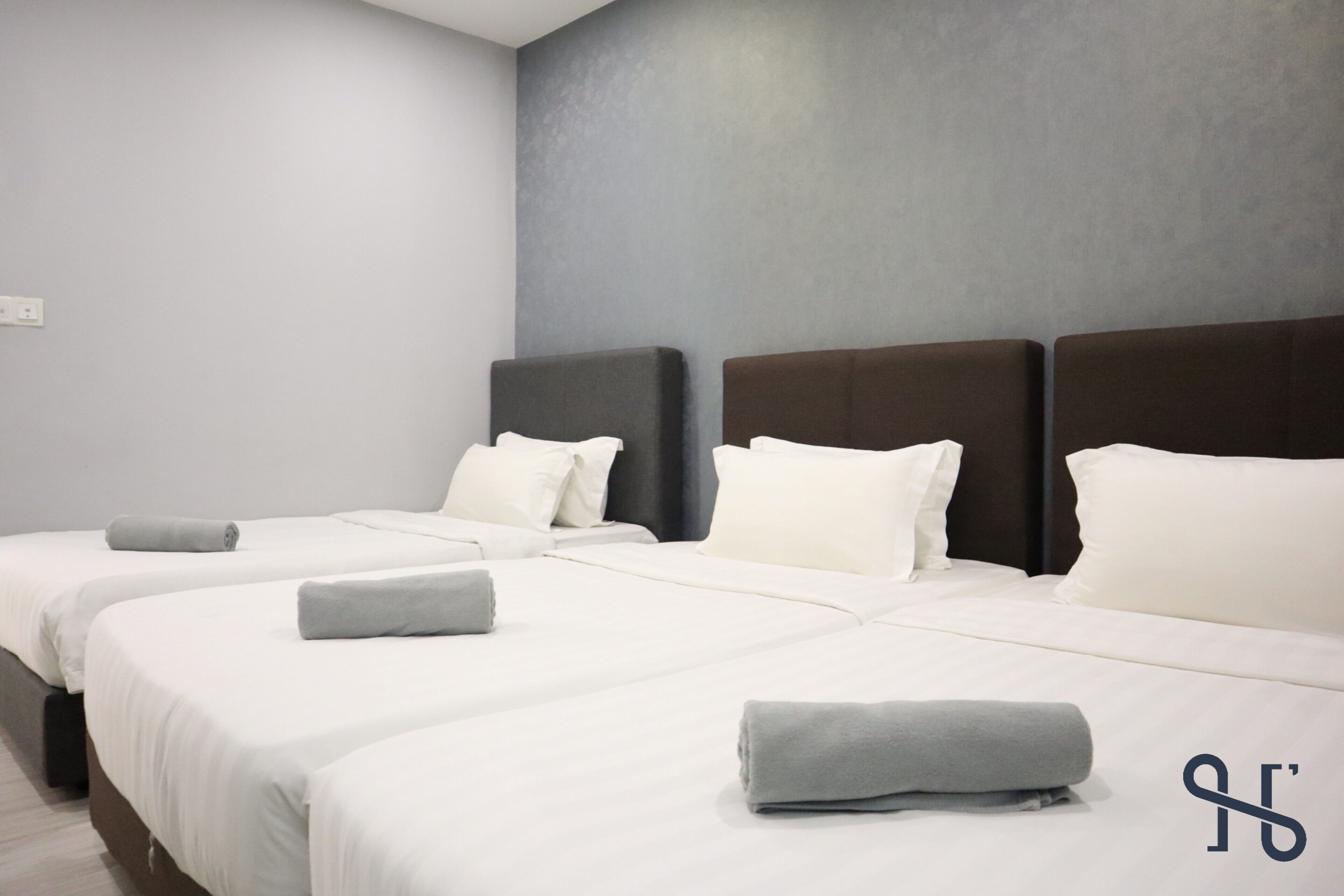 Una camera d'albergo con tre letti, ognuno con biancheria da letto bianca e asciugamani grigi.
